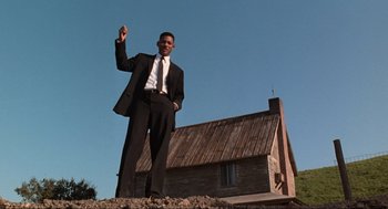 Movie still from “Men in Black” (1997), directed by Barry Sonnenfeld – A man in a suit and tie standing in front of a house; Wide shot, Low angle