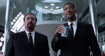 Movie still from “Men in Black” (1997), directed by Barry Sonnenfeld – Two men in suits and ties holding a cup; Medium shot, Low angle
