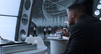 Movie still from “Men in Black” (1997), directed by Barry Sonnenfeld – A man sitting at a table with a cup of ice cream; Medium shot, Over the shoulder angle