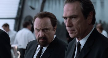 Movie still from “Men in Black” (1997), directed by Barry Sonnenfeld – Two men in suits and ties standing next to each other; Close Up shot, Over the shoulder angle