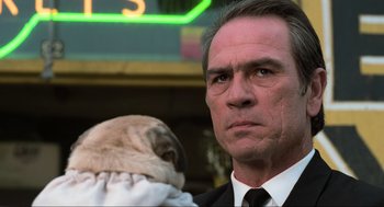 Movie still from “Men in Black” (1997), directed by Barry Sonnenfeld – A man in a suit and tie holding a pug dog; Close Up shot, Low angle
