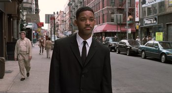 Movie still from “Men in Black” (1997), directed by Barry Sonnenfeld – A man wearing a suit and tie on a city street; Medium shot, Over the shoulder angle