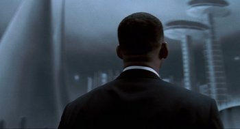 Movie still from “Men in Black” (1997), directed by Barry Sonnenfeld – A man wearing a suit and tie standing in front of a building; Close Up shot, Low angle