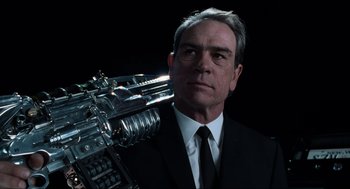 Movie still from “Men in Black” (1997), directed by Barry Sonnenfeld – A man wearing a suit and tie holding a machine gun; Close Up shot, Low angle