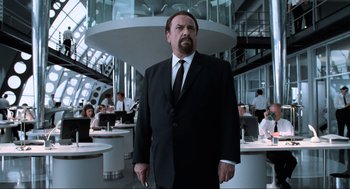 Movie still from “Men in Black” (1997), directed by Barry Sonnenfeld – A man in a suit and tie holding a cell phone; Medium shot, Low angle