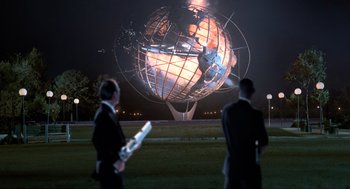 Movie still from “Men in Black” (1997), directed by Barry Sonnenfeld – Two men standing in front of a large metal globe at night; Extreme Wide shot, Over the shoulder angle