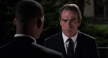 Movie still from “Men in Black” (1997), directed by Barry Sonnenfeld – A man in a suit and tie looking at another man in a suit and tie; Close Up shot, Over the shoulder angle