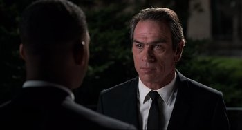 Movie still from “Men in Black” (1997), directed by Barry Sonnenfeld – A man wearing a suit and tie talking to another man; Close Up shot, Over the shoulder angle