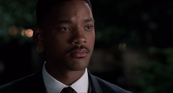 Movie still from “Men in Black” (1997), directed by Barry Sonnenfeld – A man in a suit and tie looking at the camera; Close Up shot, Over the shoulder angle