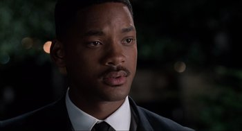 Movie still from “Men in Black” (1997), directed by Barry Sonnenfeld – A man in a suit and tie looking at the camera; Close Up shot, Over the shoulder angle