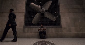 Movie still from “Men in Black 3” (2012), directed by Barry Sonnenfeld – A man sitting in front of a wall that has a fan on it; Wide shot, Overhead angle