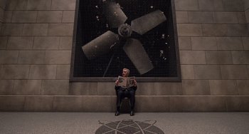 Movie still from “Men in Black 3” (2012), directed by Barry Sonnenfeld – A man sitting in front of a wall with an image on it; Wide shot, Overhead angle