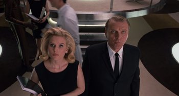 Movie still from “Men in Black 3” (2012), directed by Barry Sonnenfeld – A man and a woman standing next to each other in front of some stairs; Medium shot, Low angle