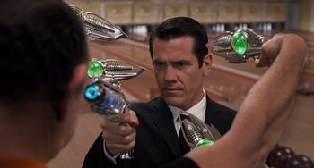 Movie still from “Men in Black 3” (2012), directed by Barry Sonnenfeld – A man in a suit and tie holding a pair of toy guns; Close Up shot, Over the shoulder angle