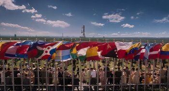 Movie still from “Men in Black 3” (2012), directed by Barry Sonnenfeld – A group of people standing next to each other with flags; Extreme Wide shot, Overhead angle