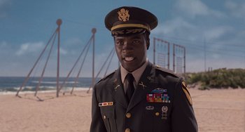 Movie still from “Men in Black 3” (2012), directed by Barry Sonnenfeld – A man in a military uniform standing in front of a sandy beach; Medium shot, Low angle