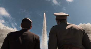 Two men in military uniforms watching a rocket launch