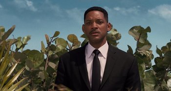Movie still from “Men in Black 3” (2012), directed by Barry Sonnenfeld – A man in a suit and tie standing next to a bush; Close Up shot, Over the shoulder angle