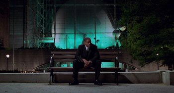 Movie still from “Men in Black II” (2002), directed by Barry Sonnenfeld – A man sitting on top of a wooden park bench; Wide shot, Low angle