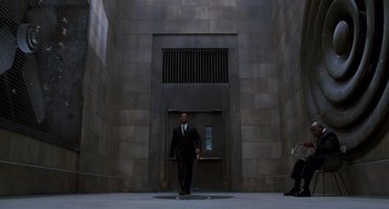 Movie still from “Men in Black II” (2002), directed by Barry Sonnenfeld – A man in a suit and tie walking in front of an elevator; Extreme Wide shot, Low angle