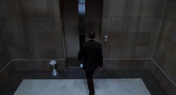 Movie still from “Men in Black II” (2002), directed by Barry Sonnenfeld – A man in a black suit walking in front of an elevator; Wide shot, High angle