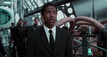 Movie still from “Men in Black II” (2002), directed by Barry Sonnenfeld – A man in a suit and tie standing in front of other men; Close Up shot, Low angle