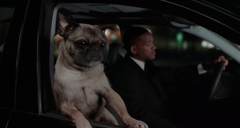 Movie still from “Men in Black II” (2002), directed by Barry Sonnenfeld – A dog sitting in the passenger seat of a car next to a man in a suit; Medium shot, Over the shoulder angle