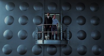 Movie still from “Men in Black II” (2002), directed by Barry Sonnenfeld – Two men and a dog standing on a balcony; Wide shot, Low angle