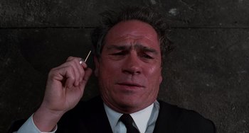 Movie still from “Men in Black II” (2002), directed by Barry Sonnenfeld – A man in a suit and tie holding a cigarette in his ear; Close Up shot, Overhead angle