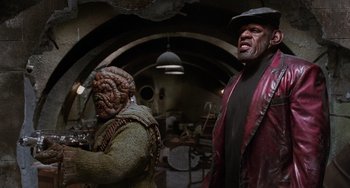 Movie still from “Men in Black II” (2002), directed by Barry Sonnenfeld – Two people in a room with a lot of stuff on the floor; Medium shot, Low angle