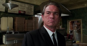 Movie still from “Men in Black II” (2002), directed by Barry Sonnenfeld – A man wearing a suit and tie in a warehouse; Close Up shot, Low angle