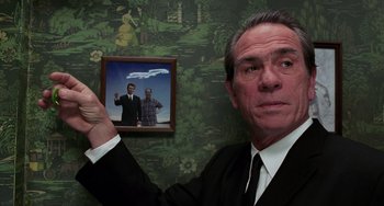 Movie still from “Men in Black II” (2002), directed by Barry Sonnenfeld – A man in a suit holding up a picture of two men; Medium shot, Over the shoulder angle