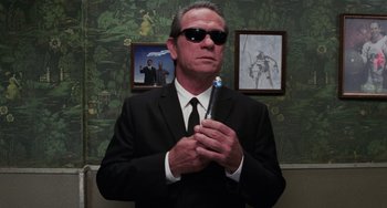 Movie still from “Men in Black II” (2002), directed by Barry Sonnenfeld – A man in a suit and sunglasses holding a toothbrush in his hands; Medium shot, Low angle