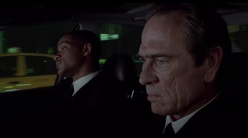 Movie still from “Men in Black II” (2002), directed by Barry Sonnenfeld – Two men in suits in the back seat of a car; Close Up shot, Over the shoulder angle