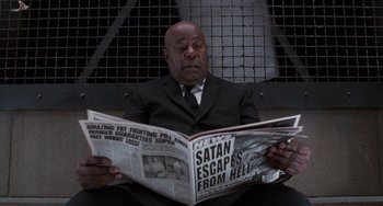 Movie still from “Men in Black II” (2002), directed by Barry Sonnenfeld – A man in a suit and tie reading a newspaper; Medium shot, High angle