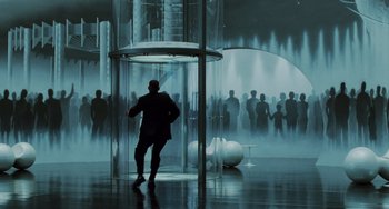 Movie still from “Men in Black II” (2002), directed by Barry Sonnenfeld – A man standing in front of a group of people in a room; Extreme Wide shot, Over the shoulder angle