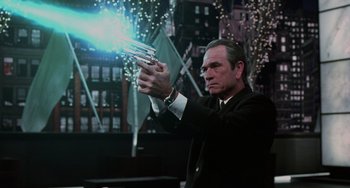 Movie still from “Men in Black II” (2002), directed by Barry Sonnenfeld – A man in a black suit and white shirt holding a gun; Medium shot, Low angle