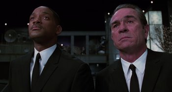 Movie still from “Men in Black II” (2002), directed by Barry Sonnenfeld – A man in a suit and tie standing next to another man in a suit and tie; Medium shot, Low angle