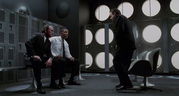 Movie still from “Men in Black II” (2002), directed by Barry Sonnenfeld – A group of men sitting in front of each other in a room; Wide shot, Low angle