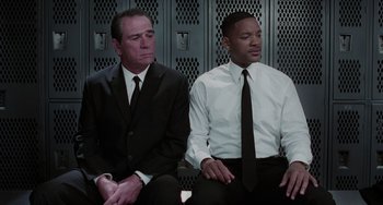 Movie still from “Men in Black II” (2002), directed by Barry Sonnenfeld – Two men sitting next to each other in front of lockers; Medium shot, Low angle