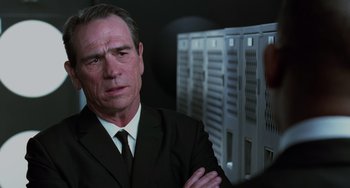 Movie still from “Men in Black II” (2002), directed by Barry Sonnenfeld – A man wearing a suit and tie standing in front of a row of lockers; Close Up shot, Over the shoulder angle