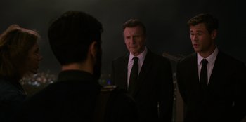 Movie still from “Men in Black: International” (2019), directed by F. Gary Gray – A man wearing a suit and tie standing in front of a microphone; Medium shot, Over the shoulder angle