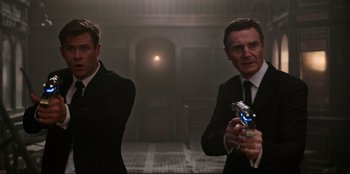 Movie still from “Men in Black: International” (2019), directed by F. Gary Gray – Two men dressed in suits and ties holding a cell phone; Medium shot, Low angle