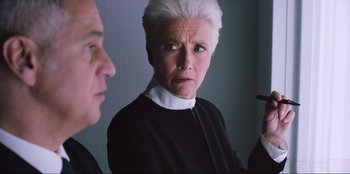 Movie still from “Men in Black: International” (2019), directed by F. Gary Gray – An older woman in a black and white dress looking at a man in a black suit; Close Up shot, Over the shoulder angle
