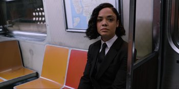 Movie still from “Men in Black: International” (2019), directed by F. Gary Gray – A woman in a suit and tie sitting on a train; Medium shot, High angle