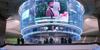 Movie still from “Men in Black: International” (2019), directed by F. Gary Gray – A group of people sitting in front of a large screen; Extreme Wide shot, Over the shoulder angle
