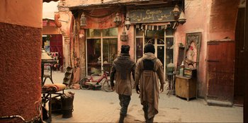 Movie still from “Men in Black: International” (2019), directed by F. Gary Gray – Two people walking down a street in front of a building; Wide shot, Over the shoulder angle