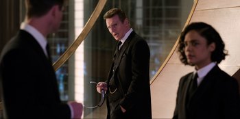 Movie still from “Men in Black: International” (2019), directed by F. Gary Gray – A man wearing a suit and tie holding a phone; Medium shot, Over the shoulder angle