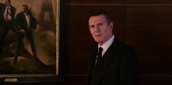 Movie still from “Men in Black: International” (2019), directed by F. Gary Gray – A man in a suit and tie in front of a painting; Medium shot, Low angle