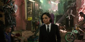 Movie still from “Men in Black: International” (2019), directed by F. Gary Gray – A man in a suit and tie standing in an industrial setting; Medium shot, Over the shoulder angle